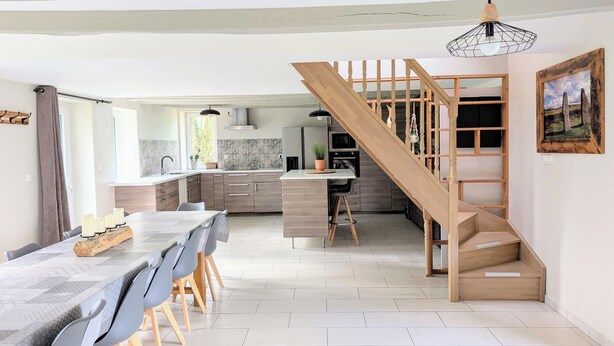 A modern kitchen with wooden cabinets, a dining area with a table and chairs, and a staircase leading to an upper level.