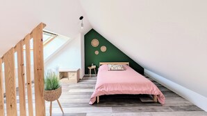 A bedroom with a sloped ceiling, a bed with a pink bedspread, a wooden floor, a green accent wall, and a skylight.