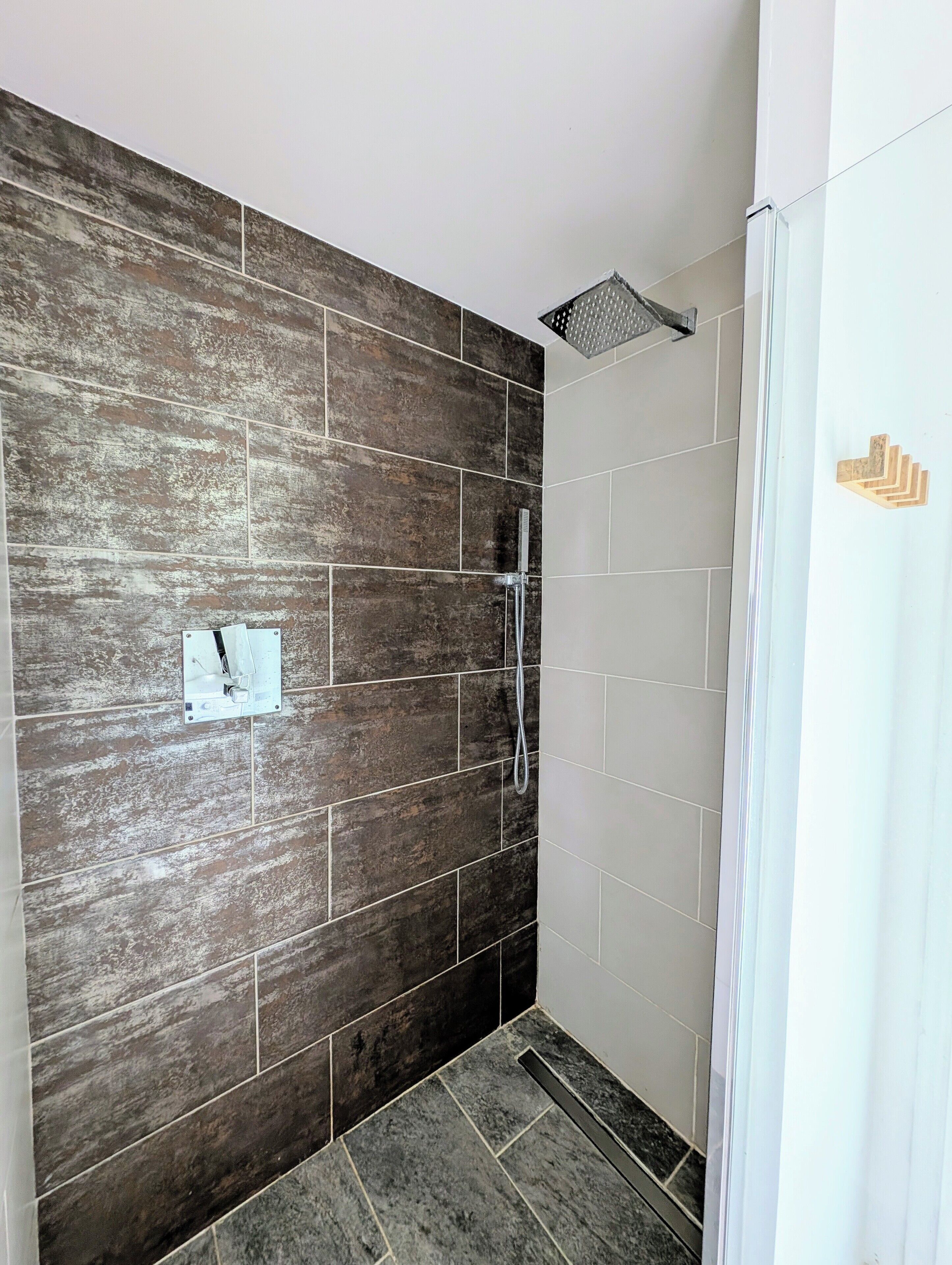 A shower area with dark stone tiles, a showerhead, and a hand symbol indicating a hand dryer.