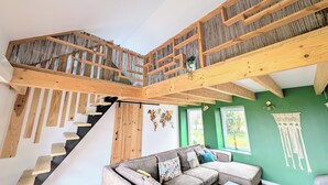 A spacious living area with a staircase leading to an upper level, a green wall, and a large sofa with cushions.