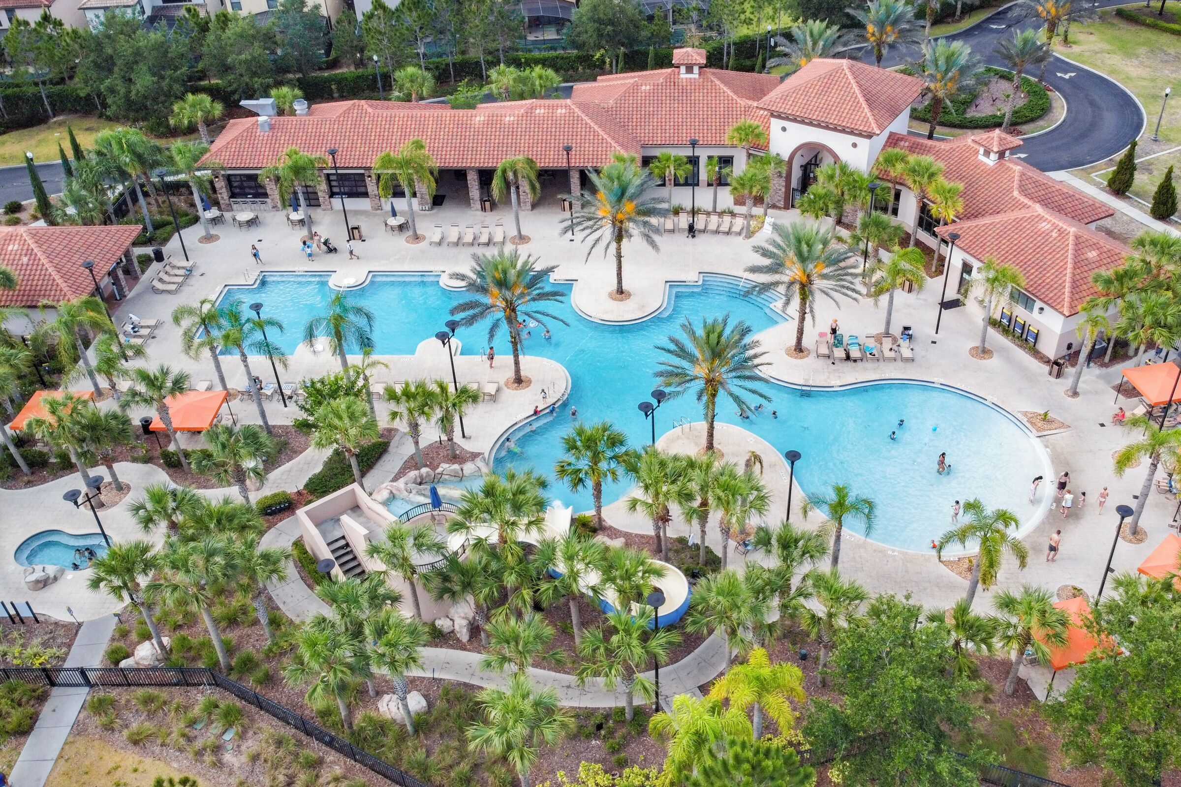 Vista aérea de un resort con múltiples piscinas, palmeras y un edificio central con techo de tejas rojas.