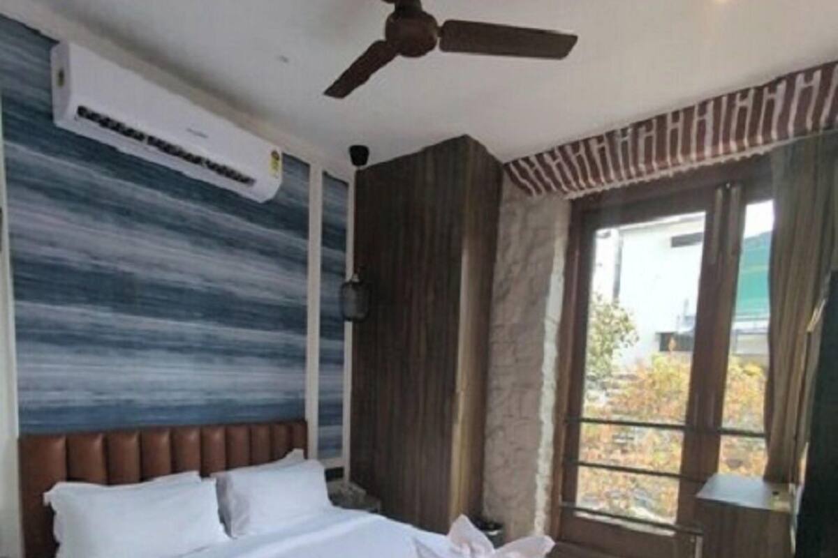 Una habitación de hotel con una cama, ventilador de techo, aire acondicionado y ventana con vista.