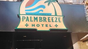 Fachada del Hotel Palm Breeze, con un letrero de temática tropical que muestra palmeras y olas.
