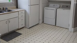 Eine kompakte Küche mit Kühlschrank, Waschmaschine und einem kleinen Fenster mit Vorhang.