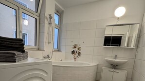 Une salle de bain moderne avec une baignoire, un lavabo, un miroir et une fenêtre.