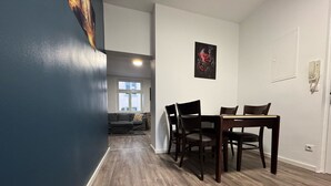 Un salon moderne avec un mur d’accent bleu foncé, un plancher en bois, un coin repas avec une table et des chaises, et un ensemble de canapés.