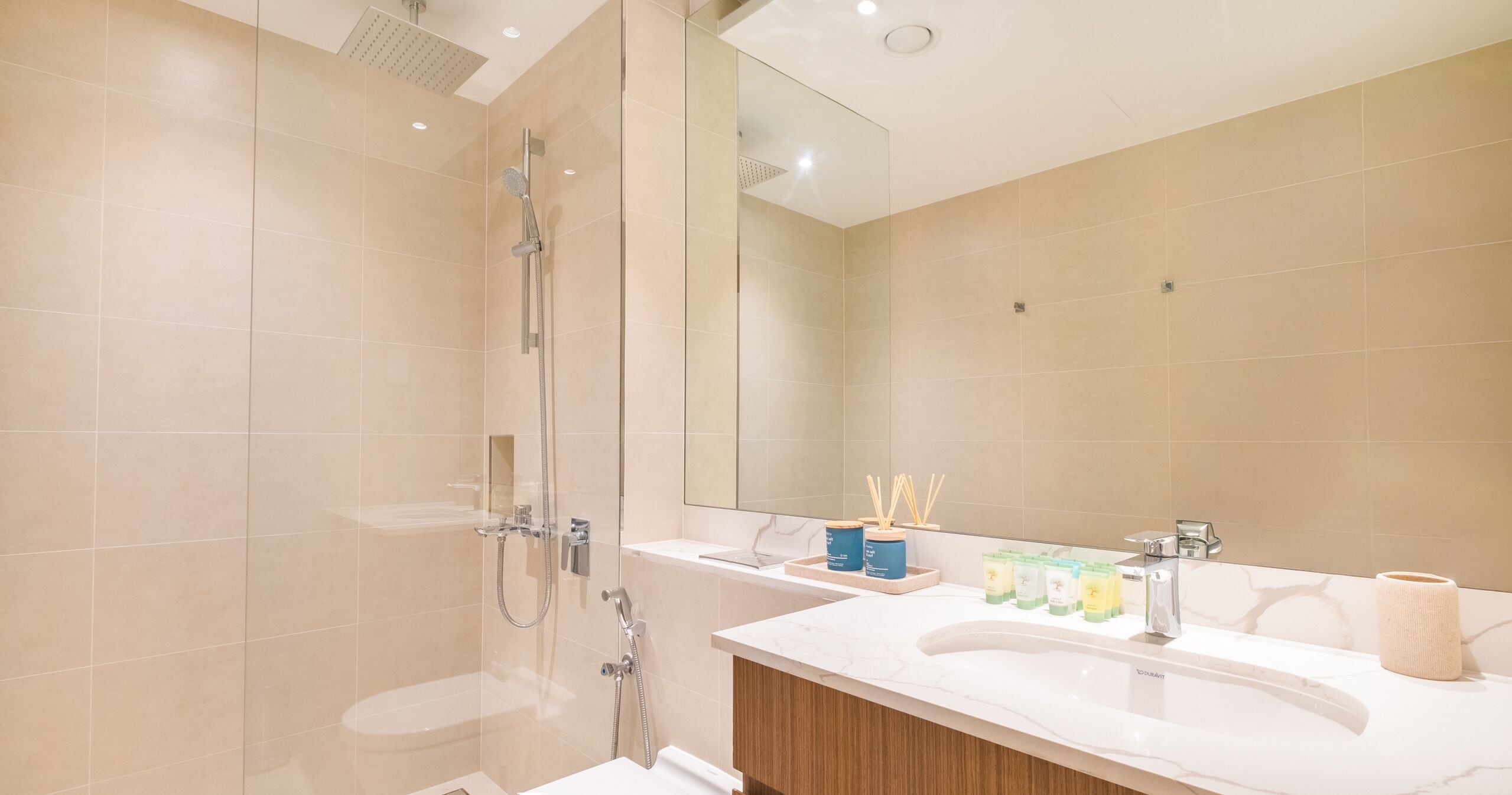 Une salle de bain moderne avec une douche à parois de verre, un grand miroir et un meuble-lavabo avec des articles de toilette.