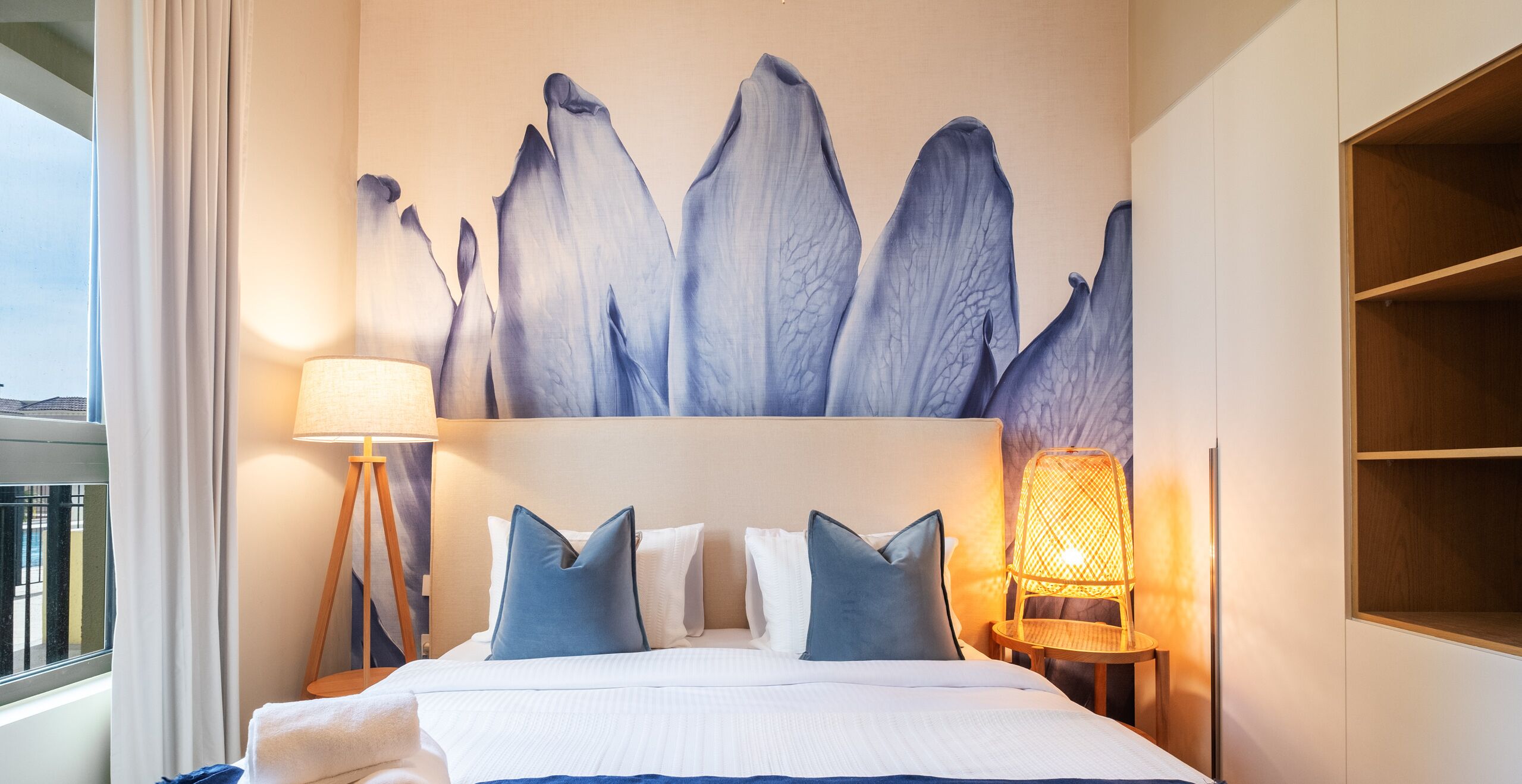 Une chambre d’hôtel comprenant un lit, des oreillers, une table de chevet, une lampe et une œuvre d’art murale.
