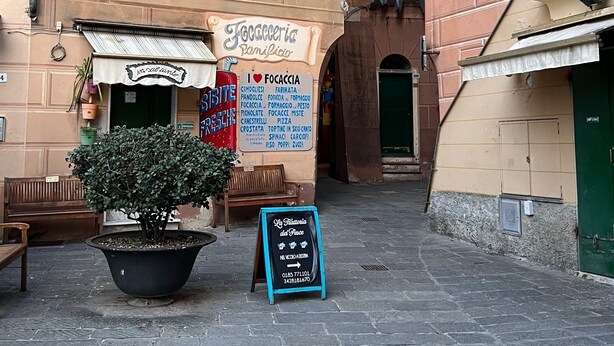 A narrow street with buildings featuring green shutters and a signboard for a restaurant.