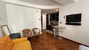 A living room with a sofa, two chairs, a TV, and a kitchen area.