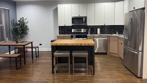 Eine moderne Küche mit weißen Schränken, einem Edelstahl-Kühlschrank, einer Mikrowelle und einem Holztisch mit zwei Hockern.