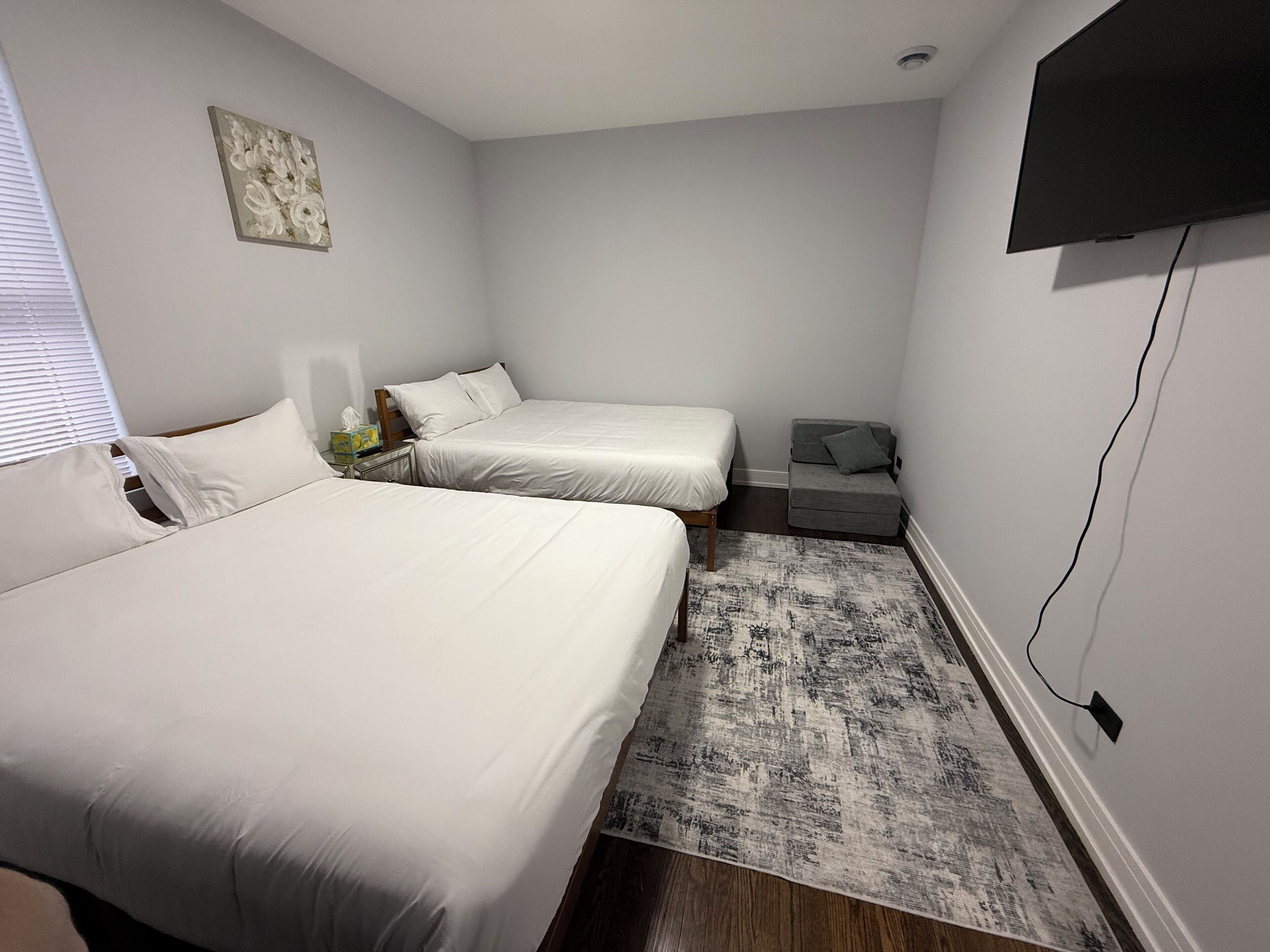 A bedroom with two beds, a small sofa, a flat-screen TV, and a painting on the wall.
