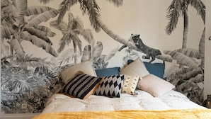 Un dormitorio con cama, almohadas y un mural en la pared que muestra una escena tropical.