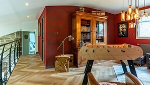 Una habitación acogedora con mesa de futbolín de madera, un sillón de cuero, estantería y pared de acento roja.