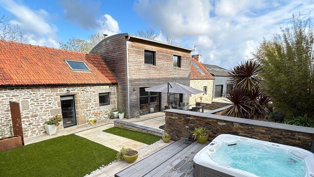 Una casa moderna con fachada de piedra, terraza de madera y jacuzzi.