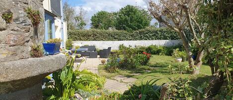 Un jardín con un banco de piedra, plantas en macetas y un patio con mobiliario exterior.