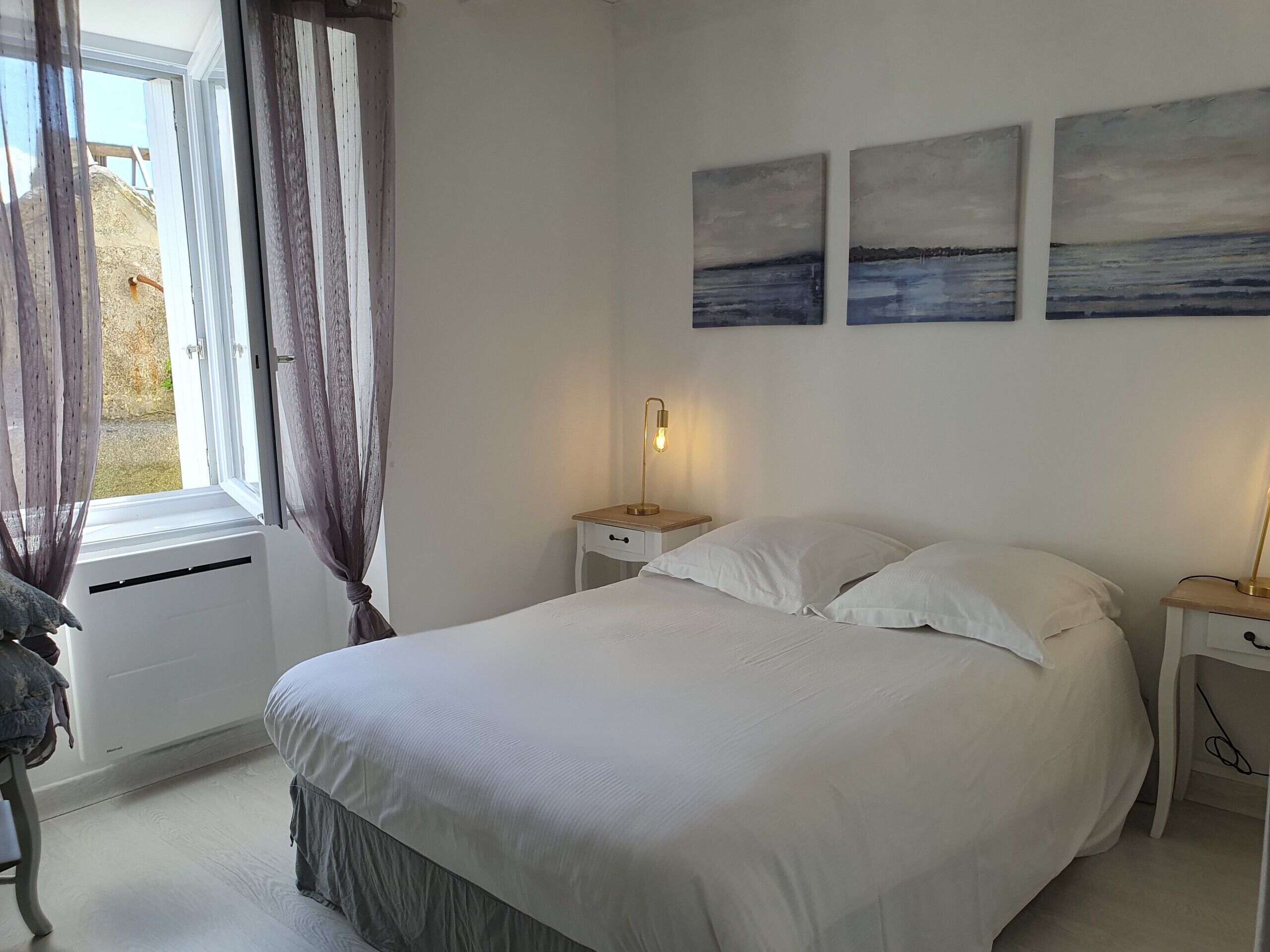 Un dormitorio con una cama, una mesita de noche, una lámpara y una ventana con cortinas.