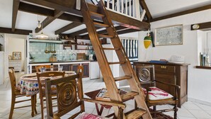 Eine rustikale Küche mit Holzbalken, einem Essbereich mit Holztisch und -stühlen sowie einer Treppe, die zu einer oberen Ebene führt.