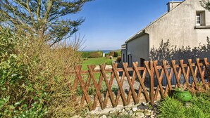 Ein rustikales Gebäude mit Natursteinfundament, Holzzaun und Blick auf das Meer.