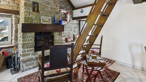 Ein rustikaler Raum mit Kamin aus Stein, einer Holzleiter und einem traditionellen Stuhl.