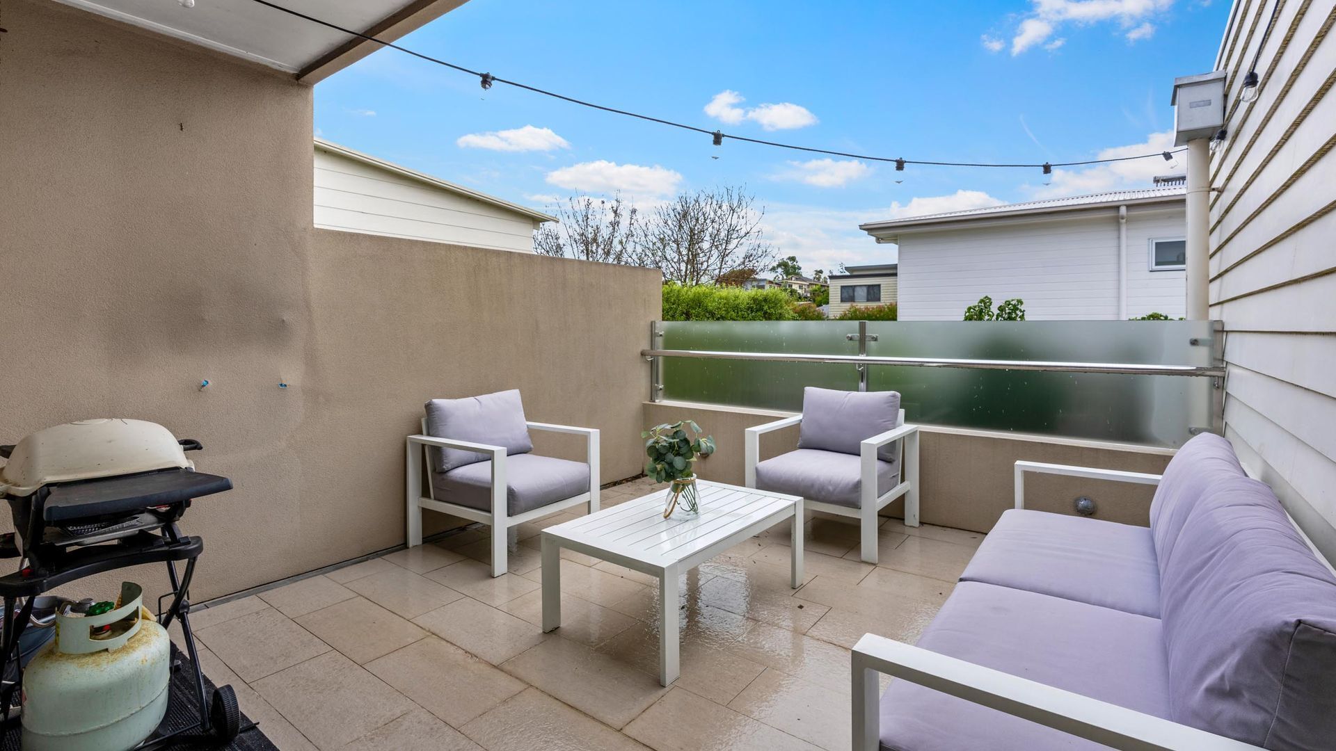 A patio area with a white table, two chairs, a sofa, and a grill.