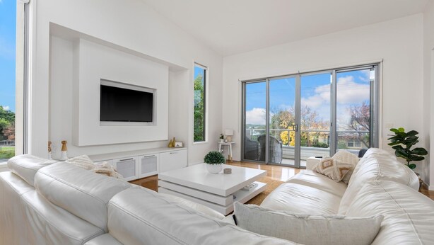 A modern living room with a white sofa, a coffee table, and a flat-screen TV mounted on the wall.