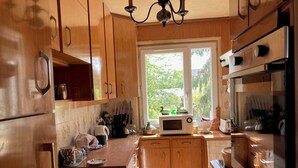 Une cuisine avec des meubles de rangement en bois, un four à micro-ondes, un évier et une fenêtre donnant sur un espace verdoyant.
