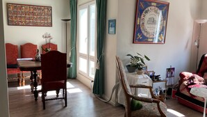Une pièce comprenant un coin repas, un canapé rouge, une chaise en bois, une table avec un vase et une carte historique encadrée accrochée au mur.