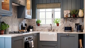 A modern kitchen with grey cabinets, a marble countertop, a built-in oven, a sink, and a window with blinds. - JOIVY Lathallan Mill Farmhouse (Leven)