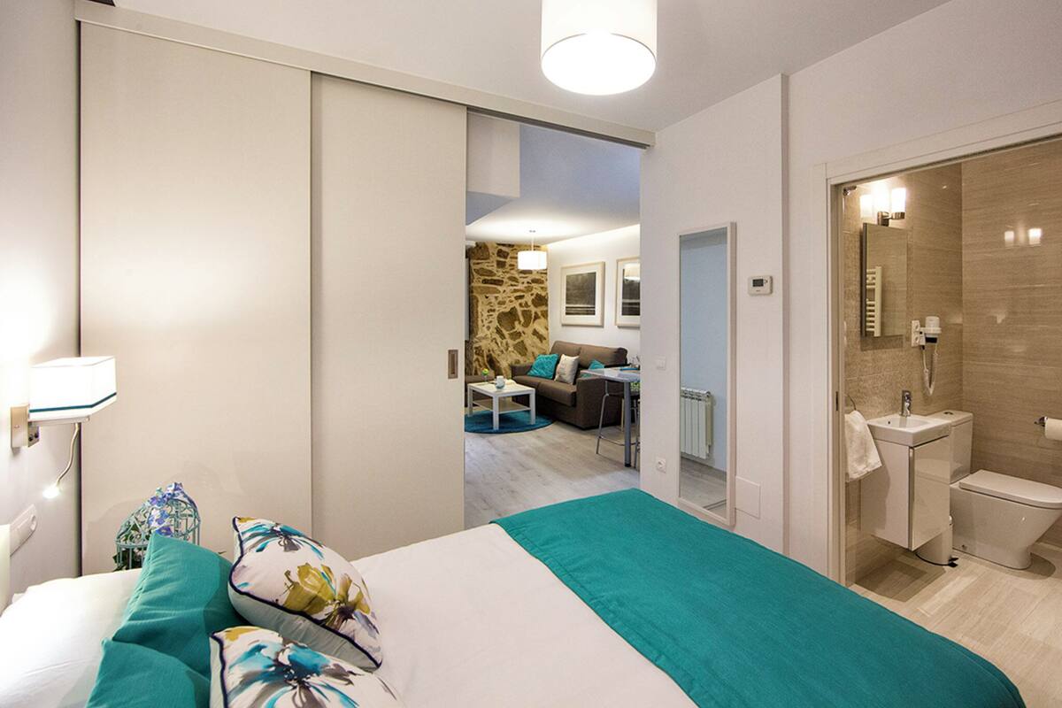 A modern bedroom with a bed, a bathroom, and a living area with a sofa and a coffee table.