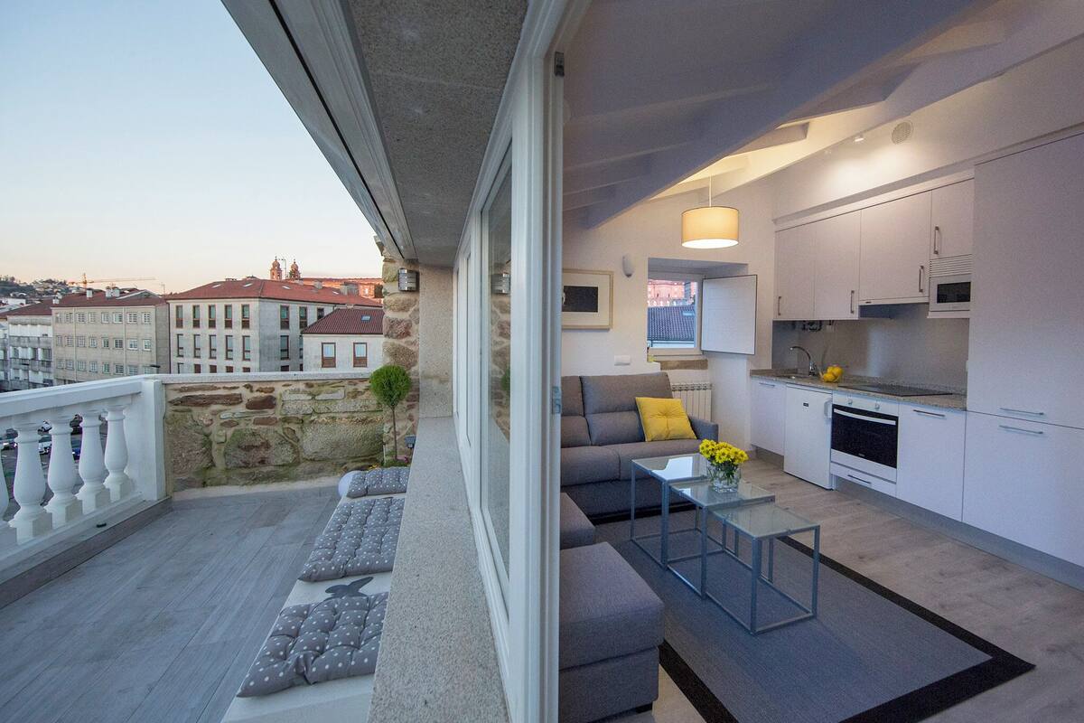 A modern apartment with a balcony, a sofa, a glass coffee table, and a kitchen area.