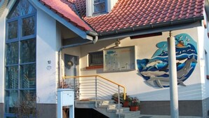 Um edifício com telhado de telhas vermelhas, um mural de golfinhos e uma escadaria com corrimão amarelo.