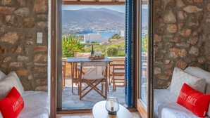 A room with stone walls, a wooden ceiling, and a view of a mountainous landscape through an open door. - Elena's Traditional DreamHouse (Paros)
