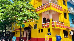 A yellow building with a red and white balcony, a tree in front, and signs for 'ShaLo's Inn' and 'RAJA BIKE RENTAL'. - Shalos Inn (Puducherry)