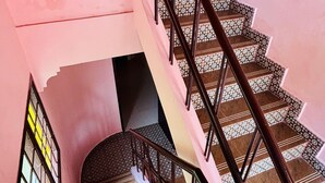 A staircase with a patterned floor and a handrail, leading to a landing with a window. - Shalos Inn (Puducherry)