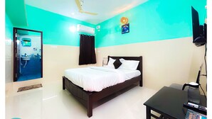 A hotel room with a bed, a desk, a ceiling fan, an air conditioning unit, and a bathroom with a sink and mirror. - Shalos Inn (Puducherry)