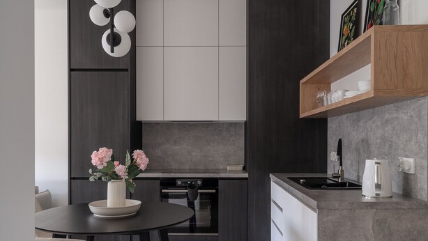 Eine moderne Küche mit dunklen Schränken, einem runden Esstisch und einer Vase mit rosa Blumen.