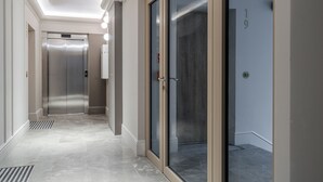 Ein moderner Flur mit Glastür, einem Metallaufzug und einem gefliesten Boden.
