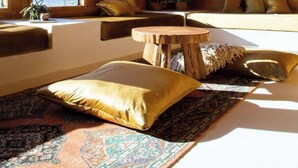 A cozy cabin interior with a wooden ceiling, large windows, a round wooden table, and a patterned rug.