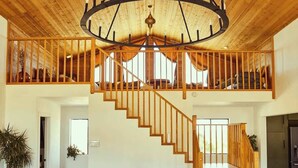 A spacious living room with a large green sofa, a wooden coffee table, and a wooden staircase leading to an upper level.