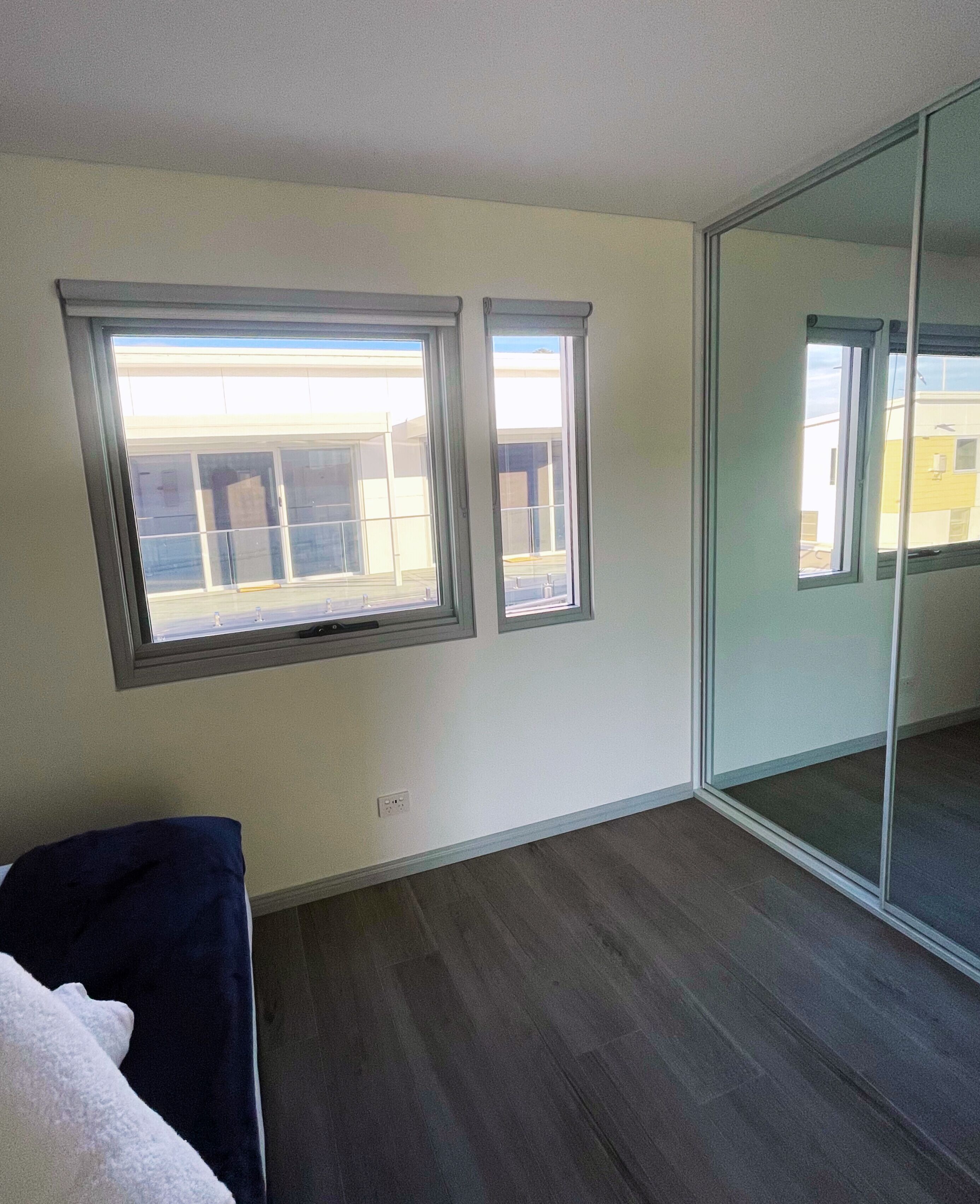 A room with two windows, a sliding glass door, and a dark wood floor.