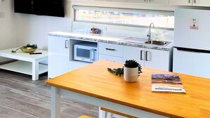 A modern kitchen with white cabinets, a wooden dining table, and a bench. - Resort on Cedar (Windang)