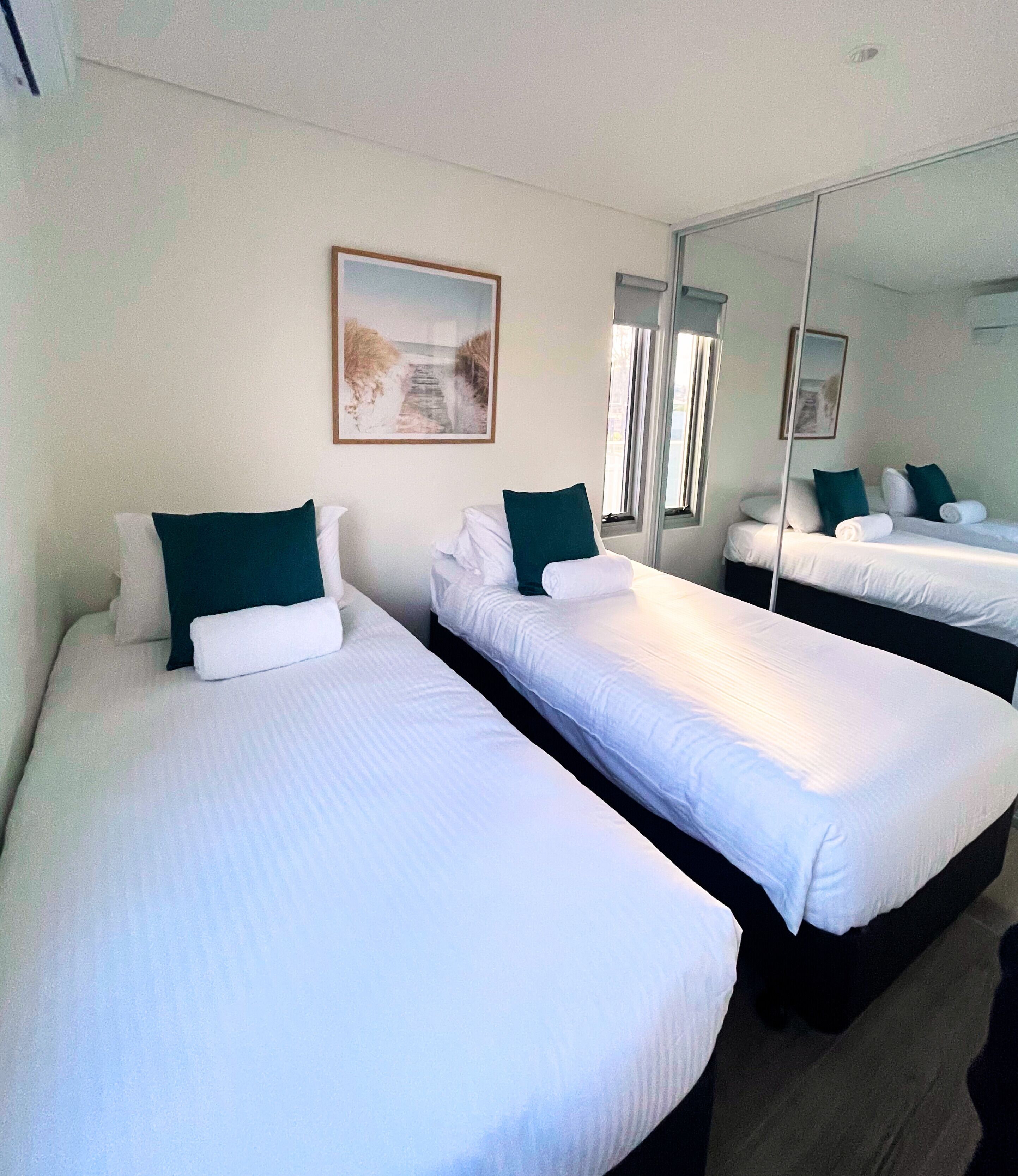 A hotel room with two single beds, a large mirror, and a painting on the wall.