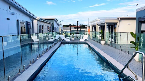 A rectangular pool with glass railings on both sides, surrounded by a wooden deck. - Resort on Cedar (Windang)