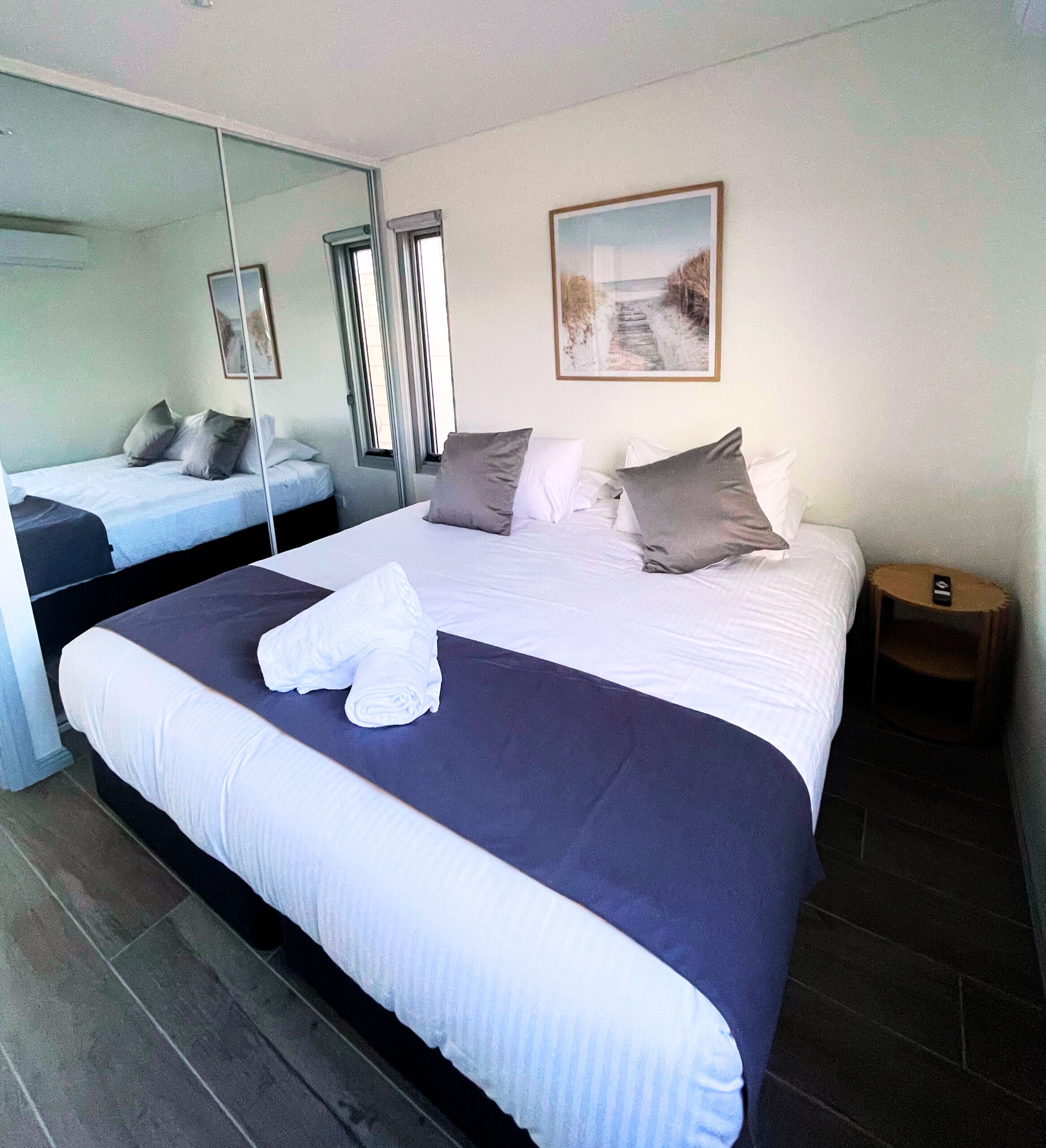 A hotel room with a large bed, a bedside table, a mirror, and a painting on the wall.