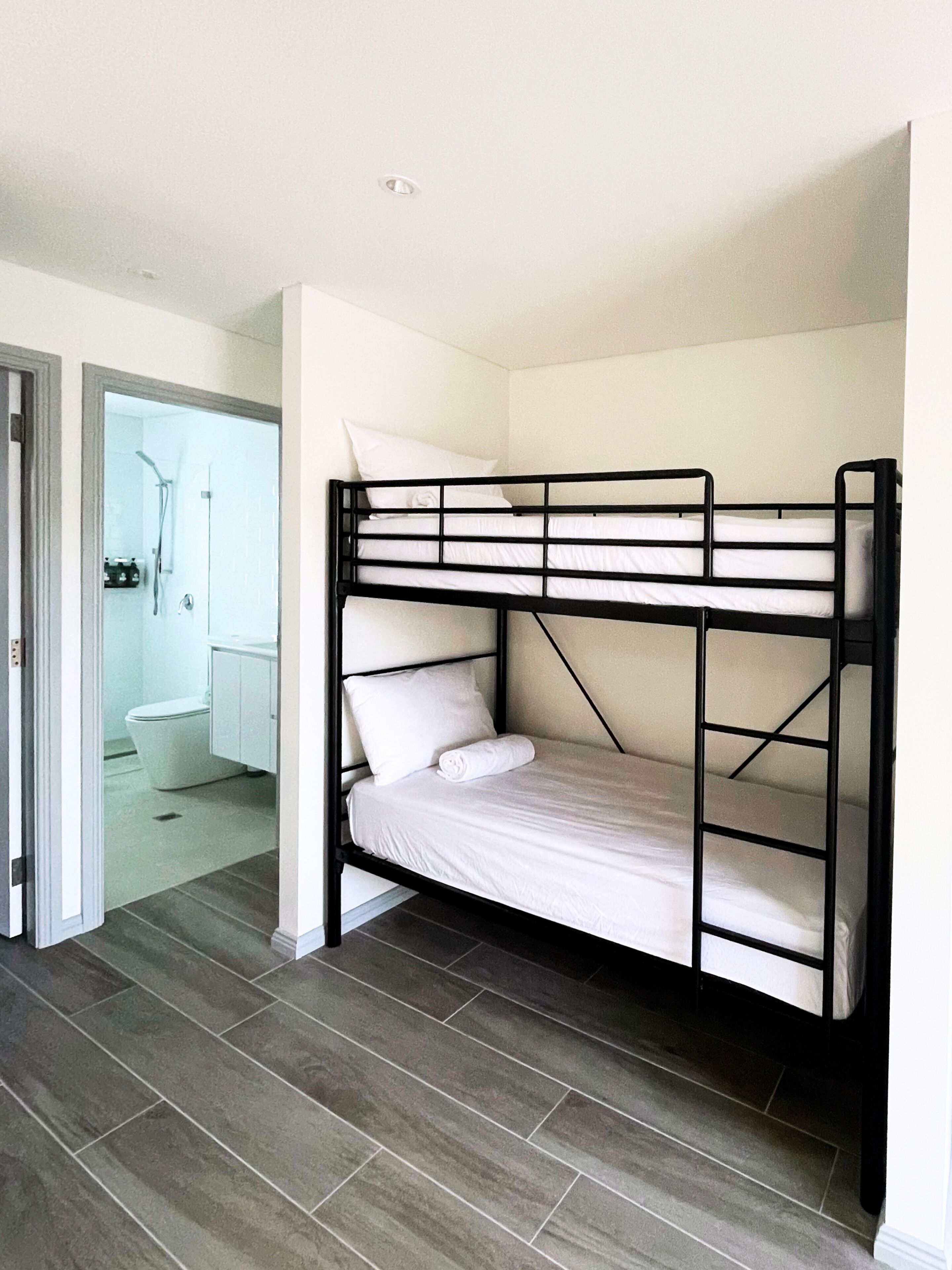 A bunk bed with white bedding in a room with grey flooring and a white door leading to a bathroom.