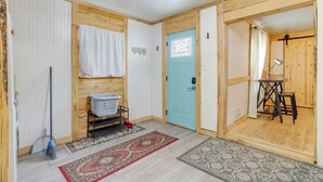 Ein Zimmer mit Holzwänden, einer blauen Tür, einem Wäschekorb, einem Tisch mit Stühlen und einem gemusterten Teppich.