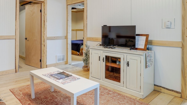 Ein Zimmer mit einem weißen Tisch, einem Fernseher auf einem Schrank und einer Tür zu einem weiteren Raum.