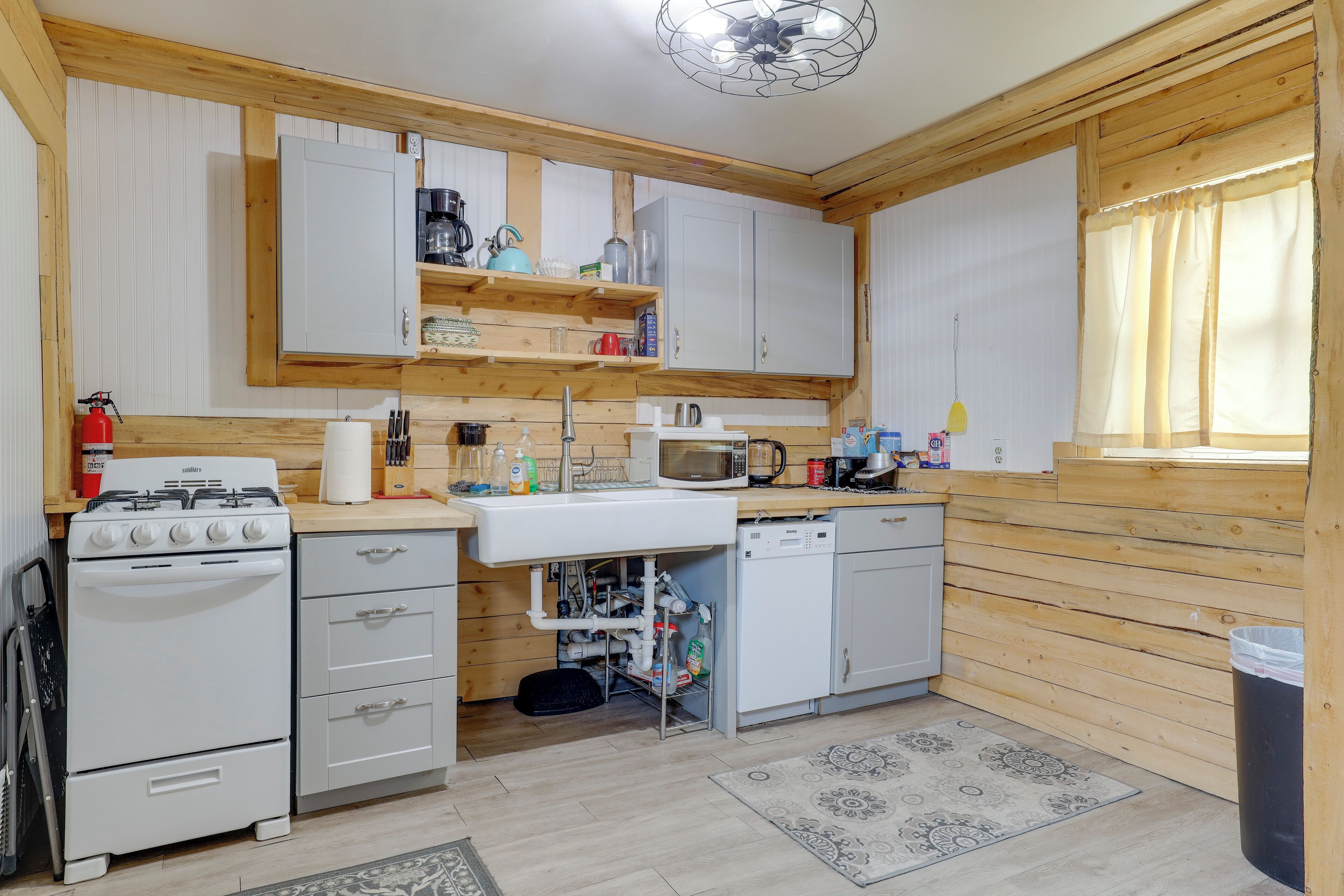 Une cuisine de taille réduite avec des murs en bois, une cuisinière à gaz, un four à micro-ondes et des armoires blanches.