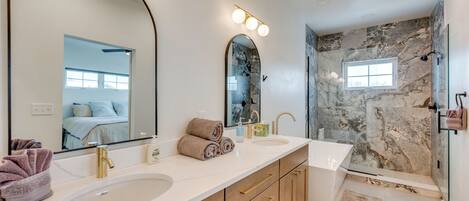 Et moderne badeværelse med to håndvaske, et stort spejl og en brusekabine med glasdør.